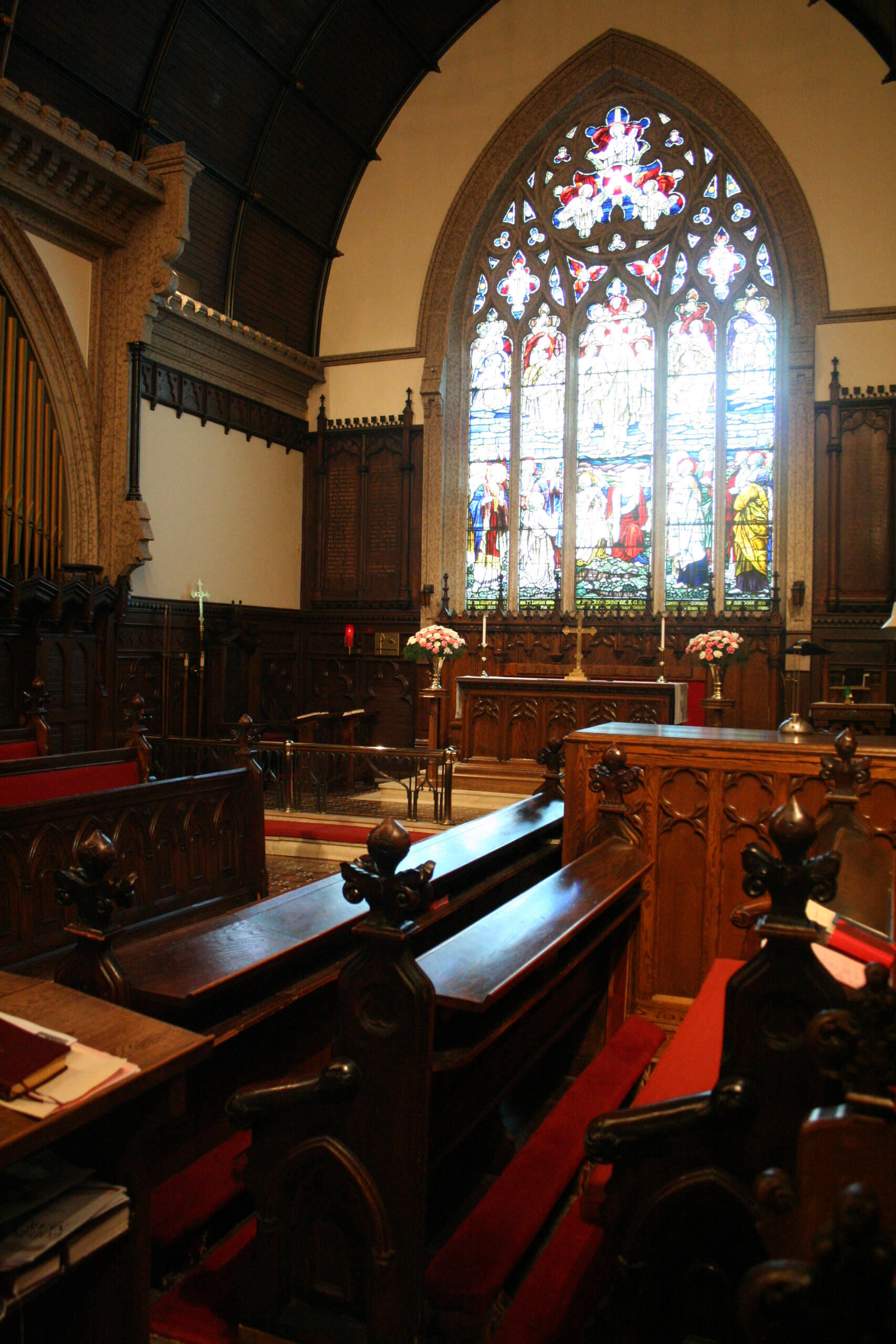 A photo of the chancel of Holy Trinity Anglican Church showing choir pews, the organ console, high altar, and great east window of the church.