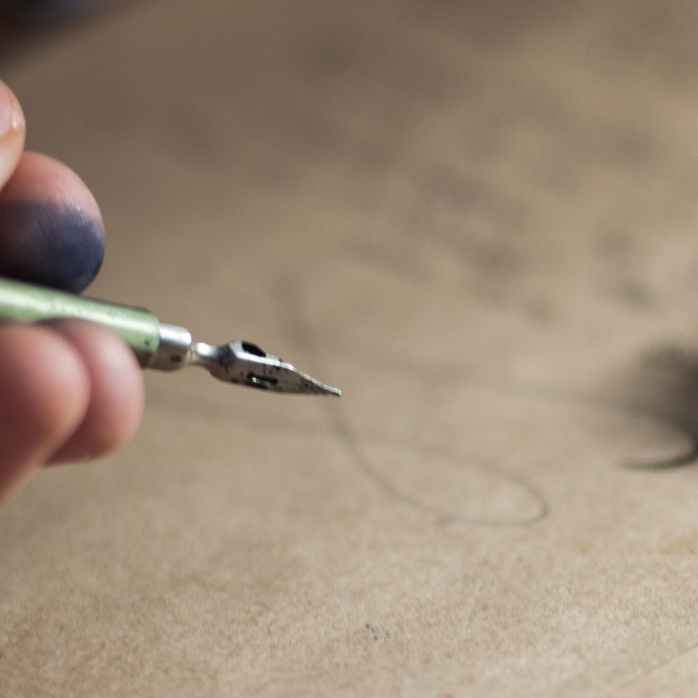 An image of ink-stained fingers holding a dip pen over a freshly-composed manuscript.